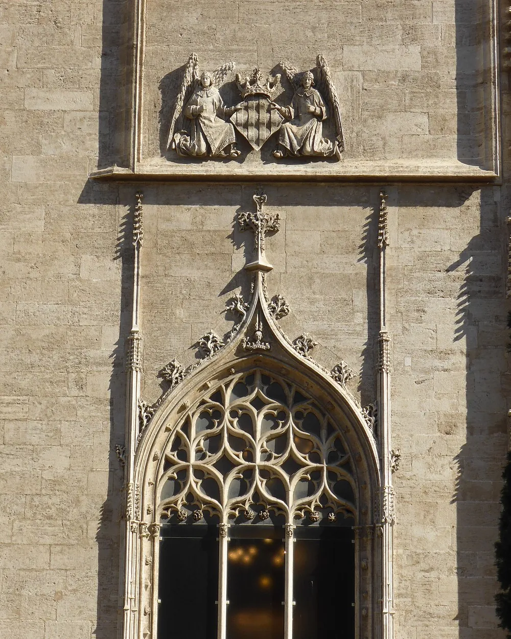 A Gothic traceried window and a carved coat of arms on the stone facade of the Lonja de la Seda in Valencia, with a street lamp beside it