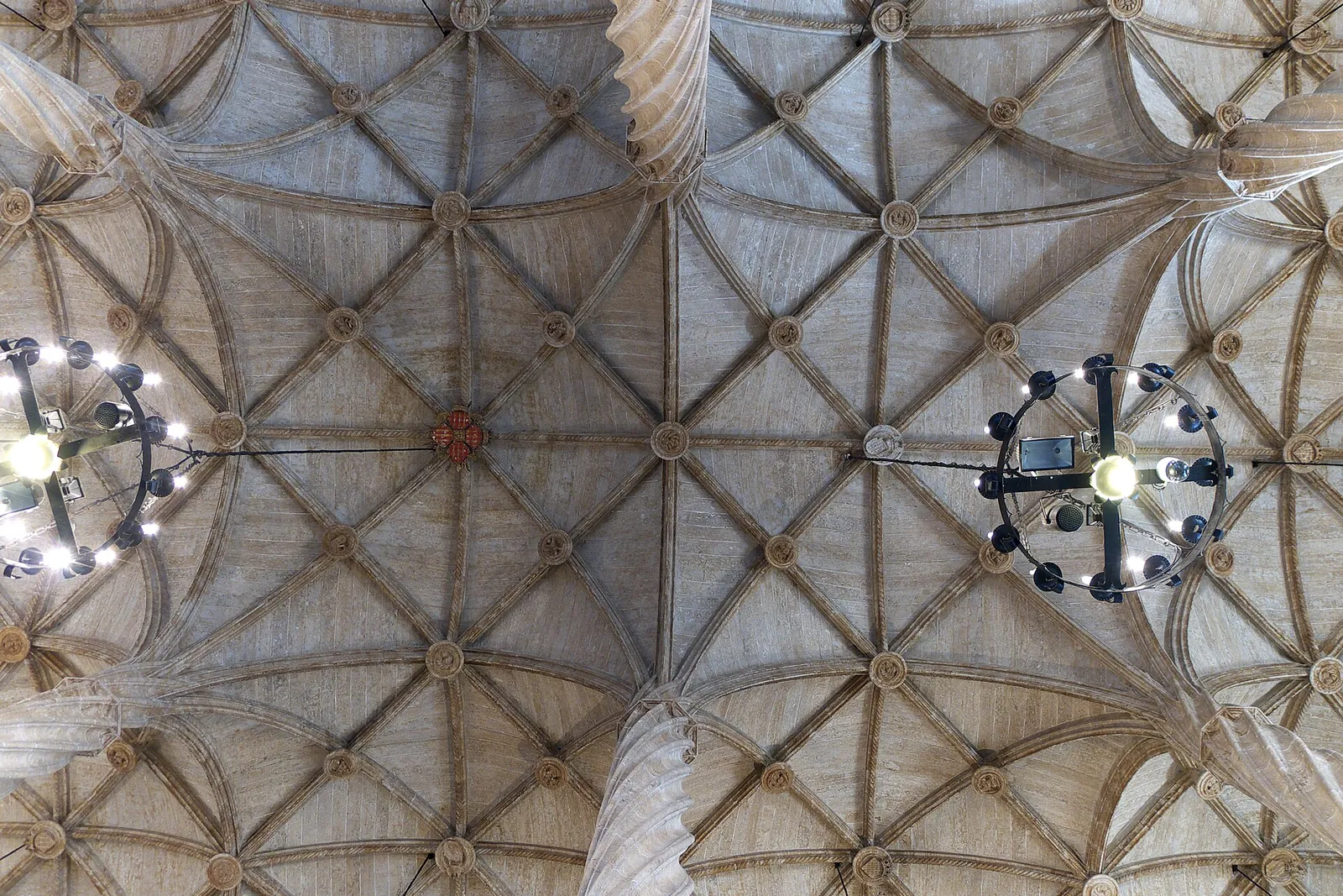 The star-ribbed stone vault of the Lonja de la Seda in Valencia, with twisted columns rising to the ceiling and two lit chandeliers